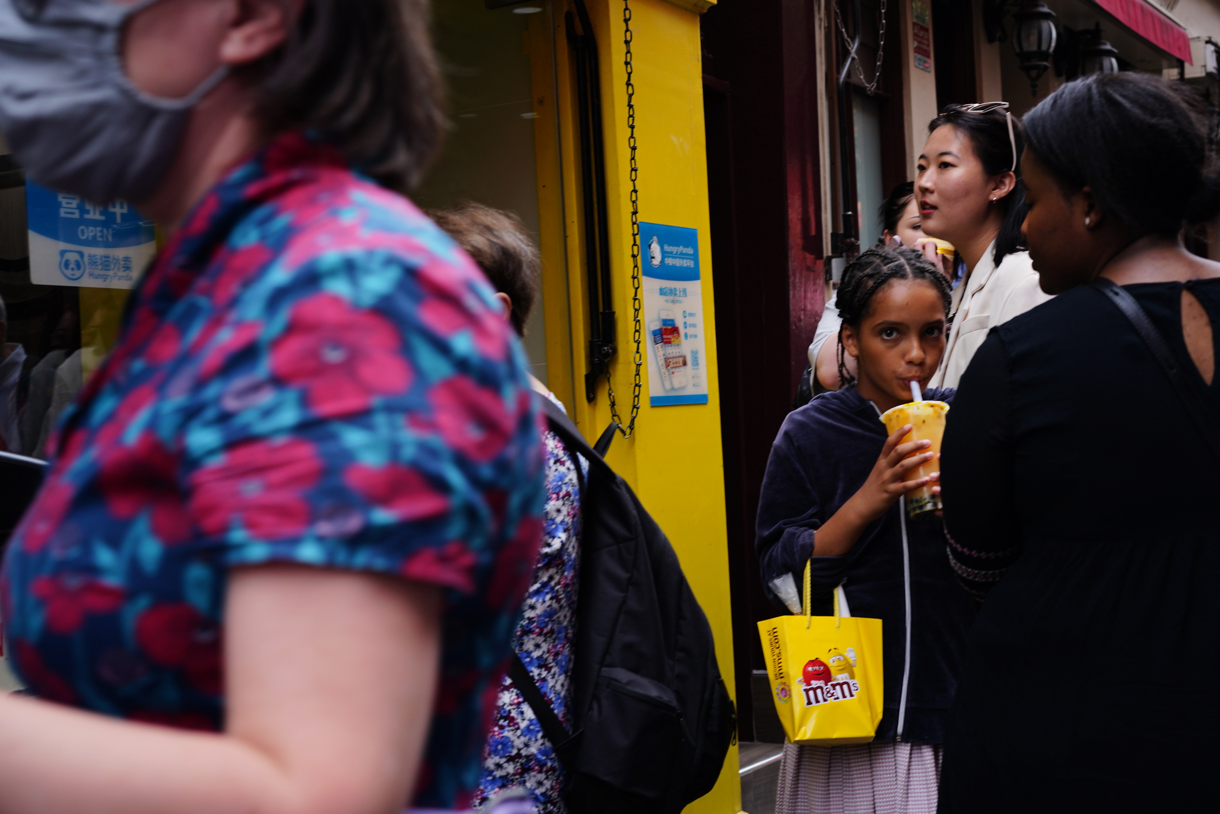 A girl looks toward the camera between passing figures and a yellow doorway.
