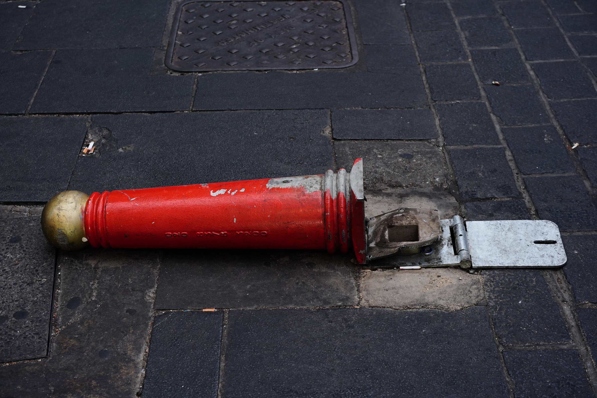 A red hinged bollard lies horizontally against grey paving.