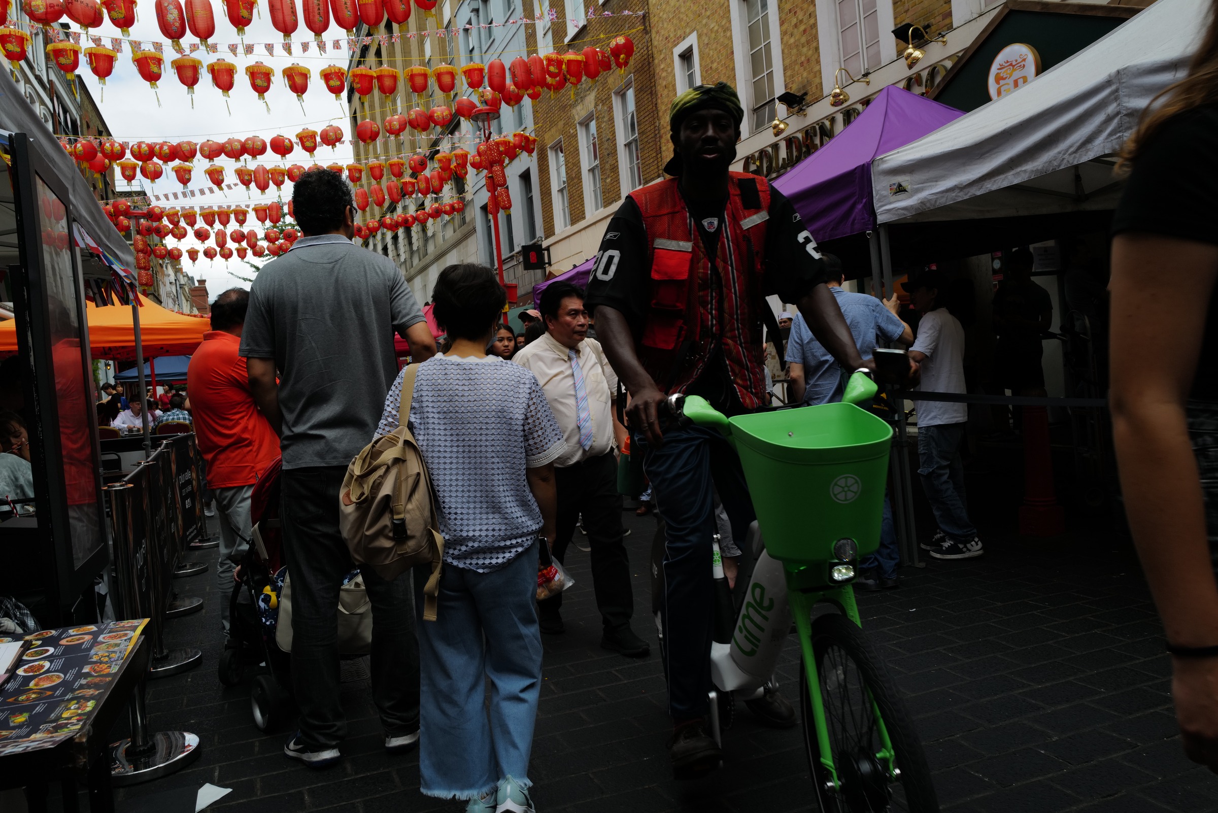 A person with a green bicycle approaches through a crowded street beneath red lanterns.