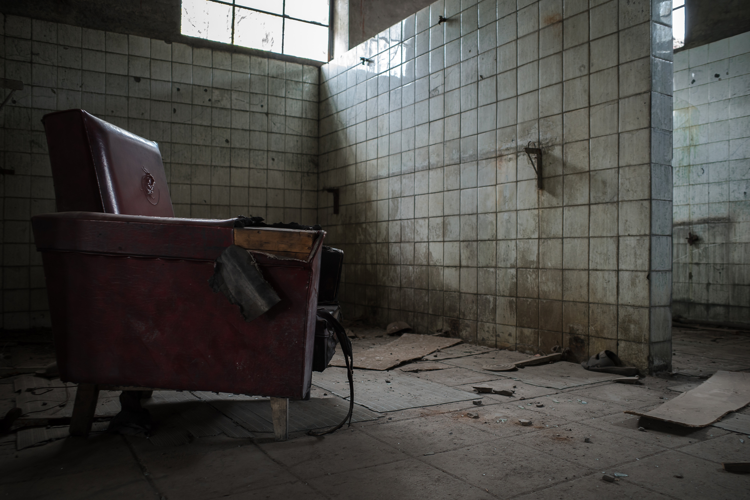 A dark red armchair stands in a tiled room, beside an empty stretch of floor.