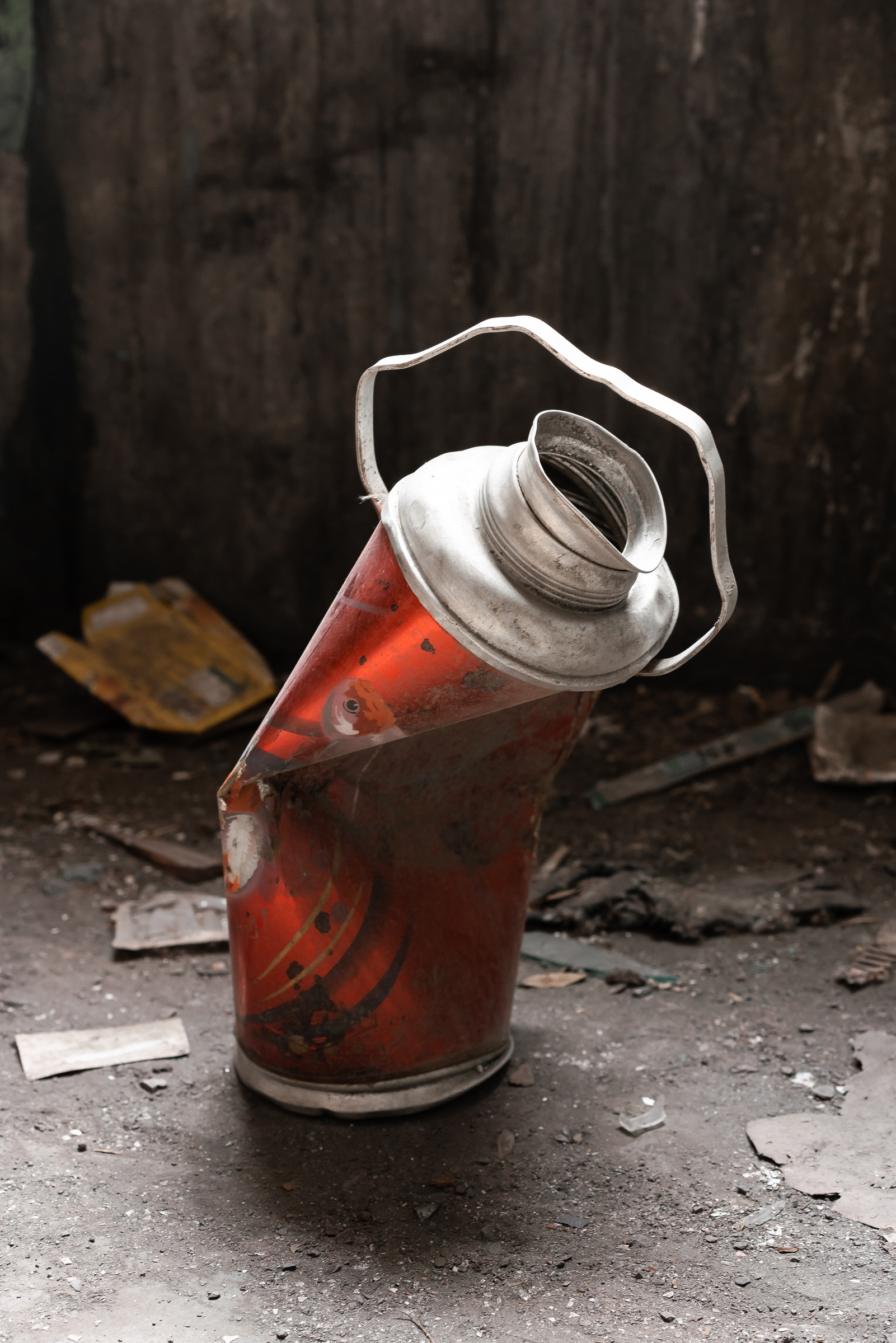 A red thermos flask, bent sharply at its middle, stands upright among fragments on the floor.
