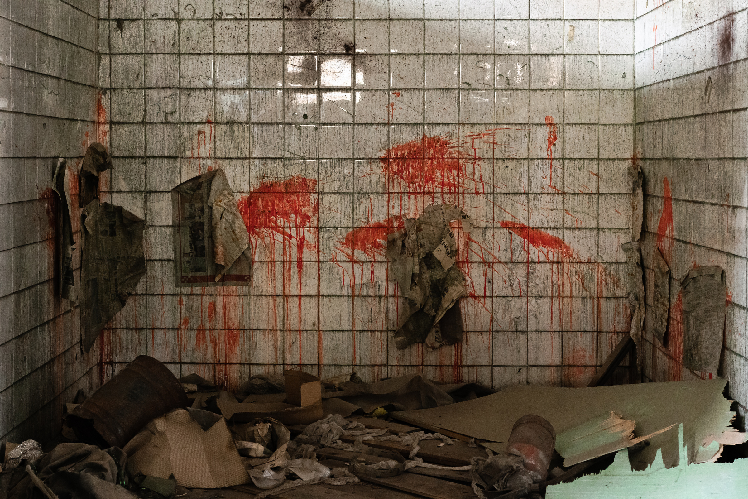 Red marks and hanging scraps of newspaper interrupt a tiled wall above a pile of debris.