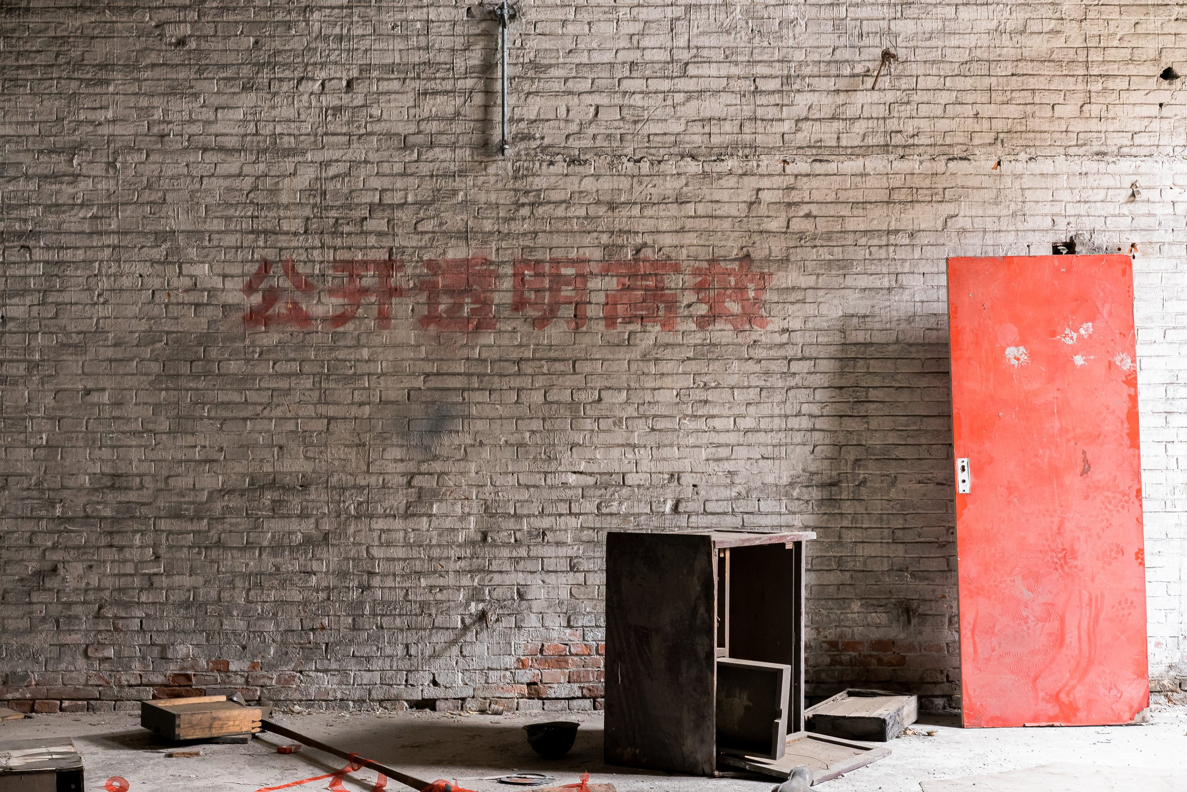 A detached red door and a small empty cabinet stand against a broad brick wall with faded lettering.
