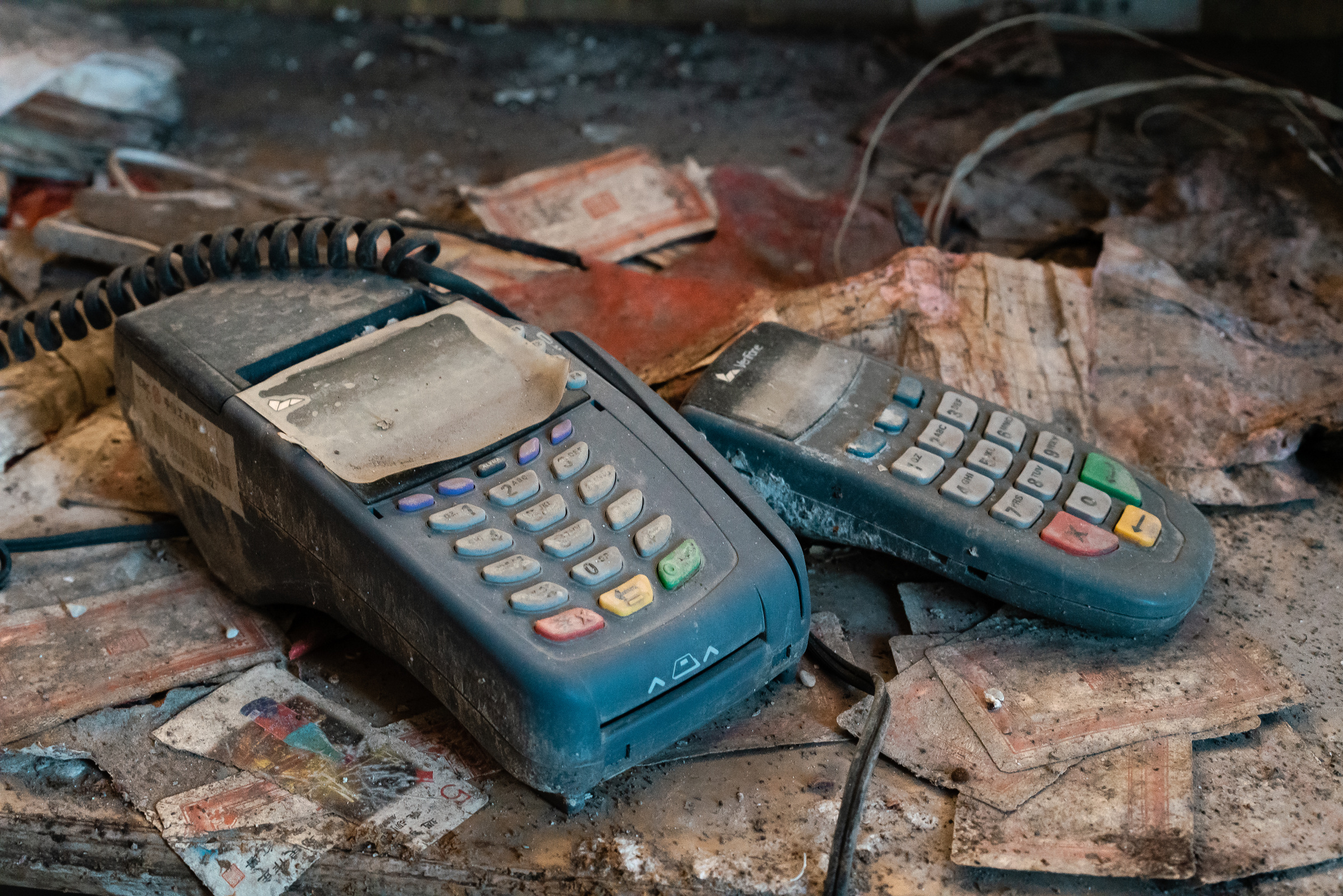 Two blue payment terminals rest on scattered papers and debris.