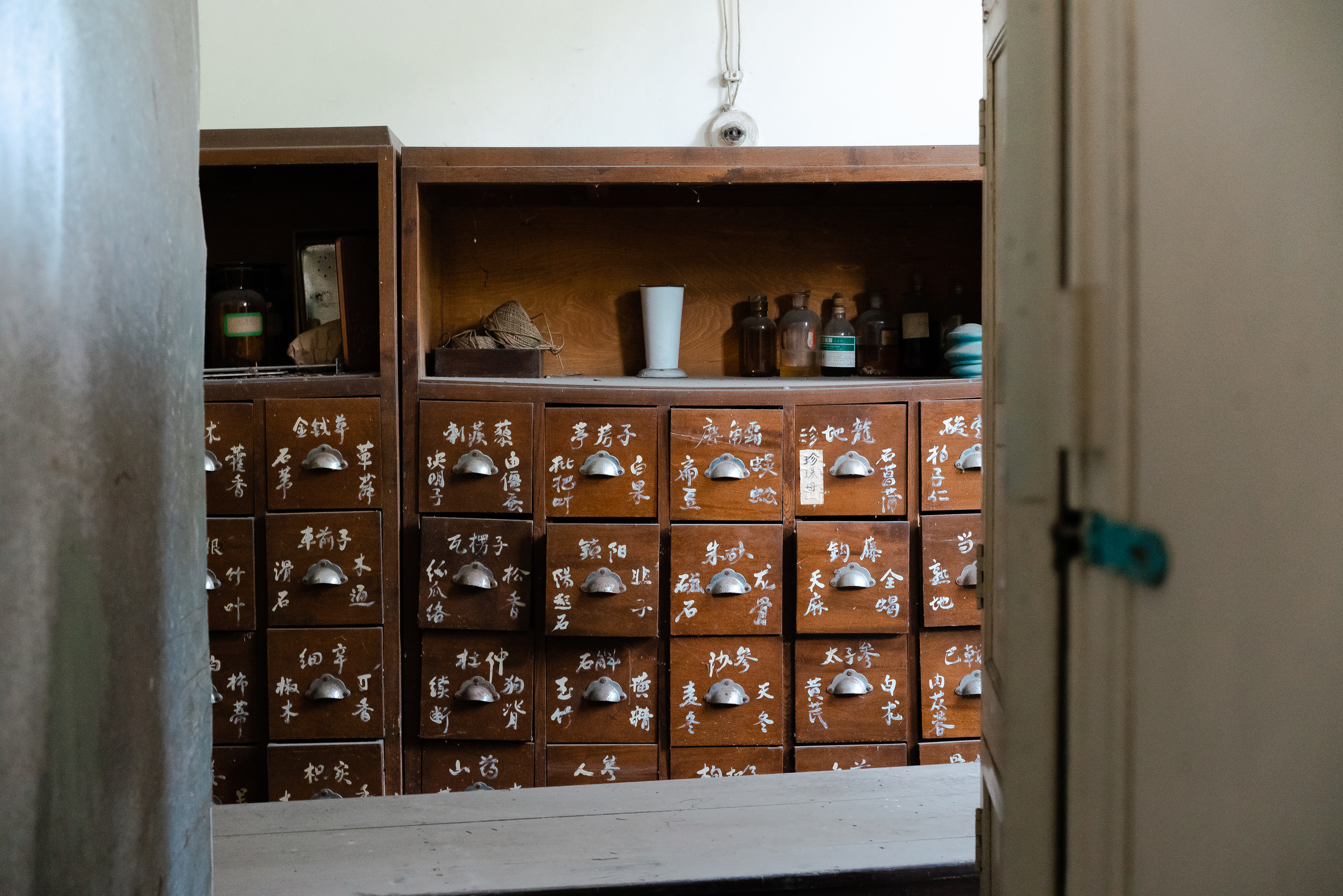 An apothecary cabinet with handwritten labels is seen through an open doorway.