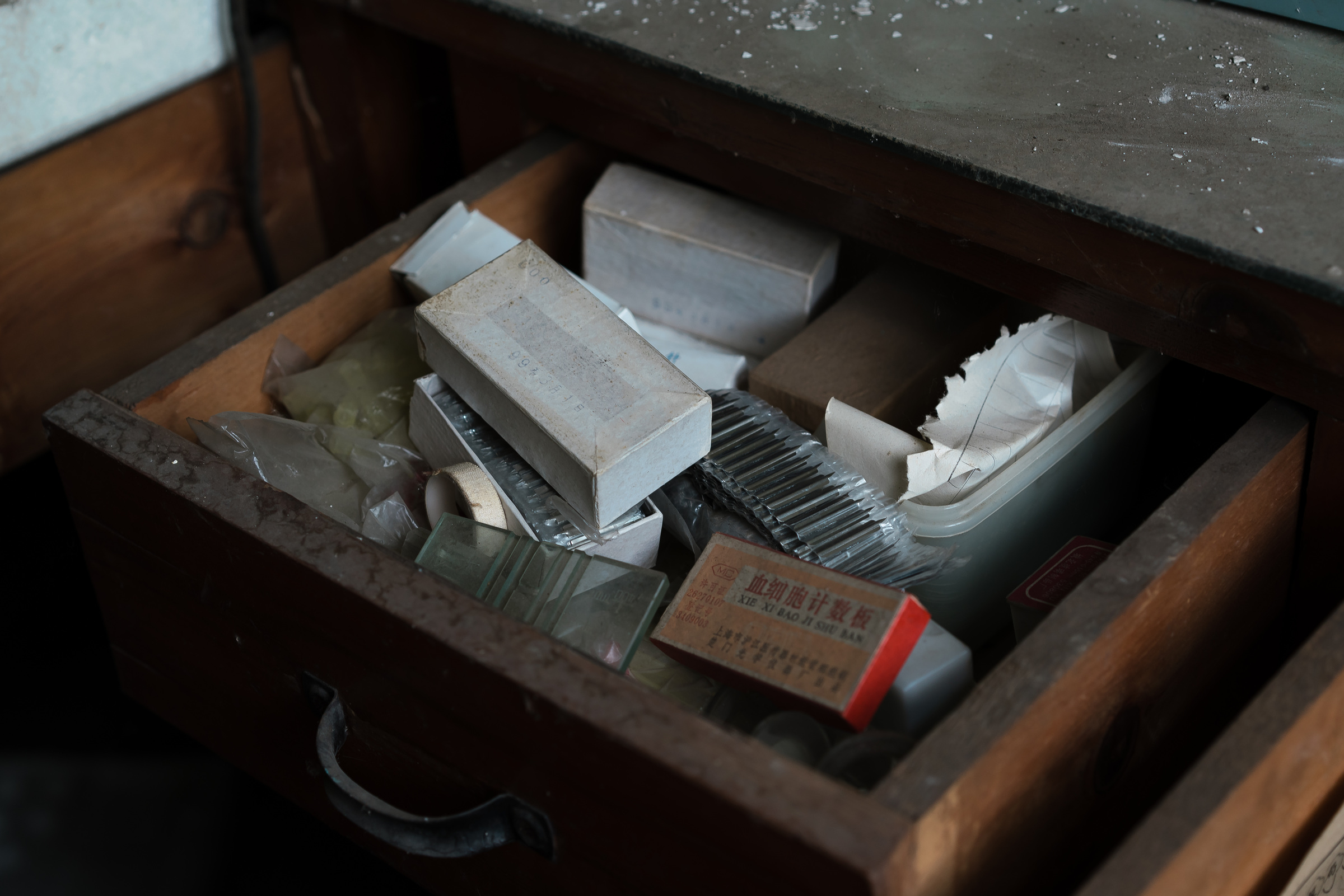 An open wooden drawer contains small boxes, glass pieces and laboratory instruments.