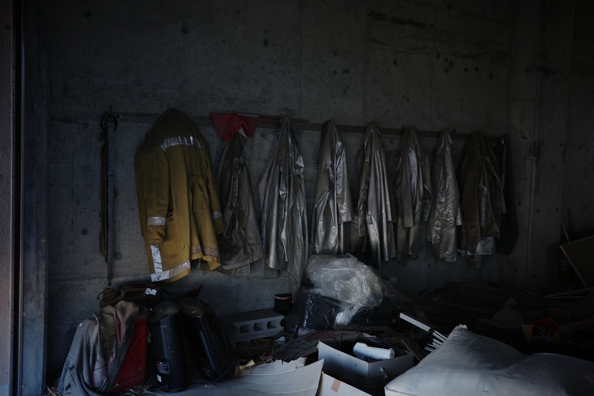 Firefighting jackets hang along a wall above scattered debris.