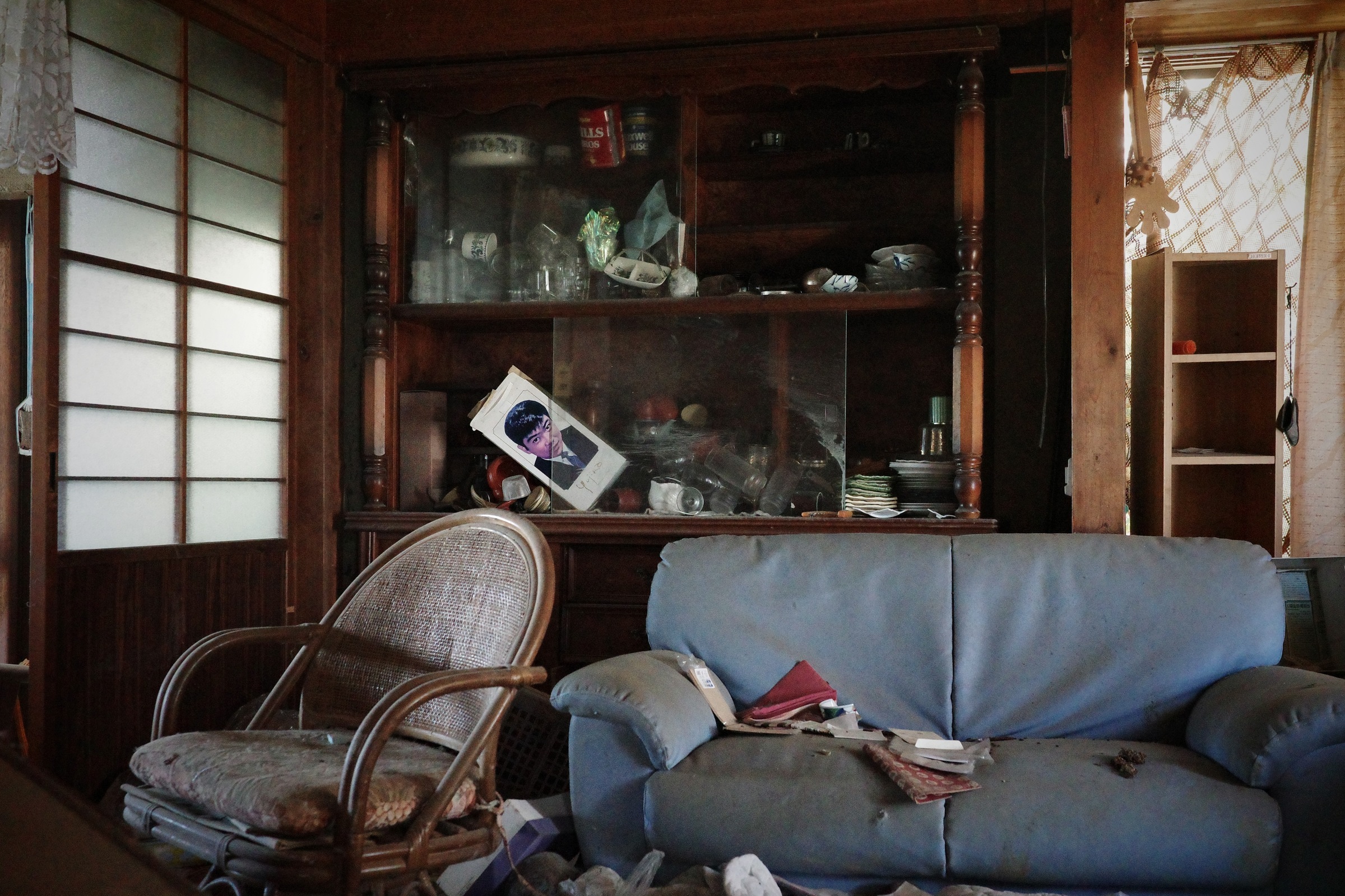 A blue sofa and wicker chair sit in front of a dark wooden display cabinet.