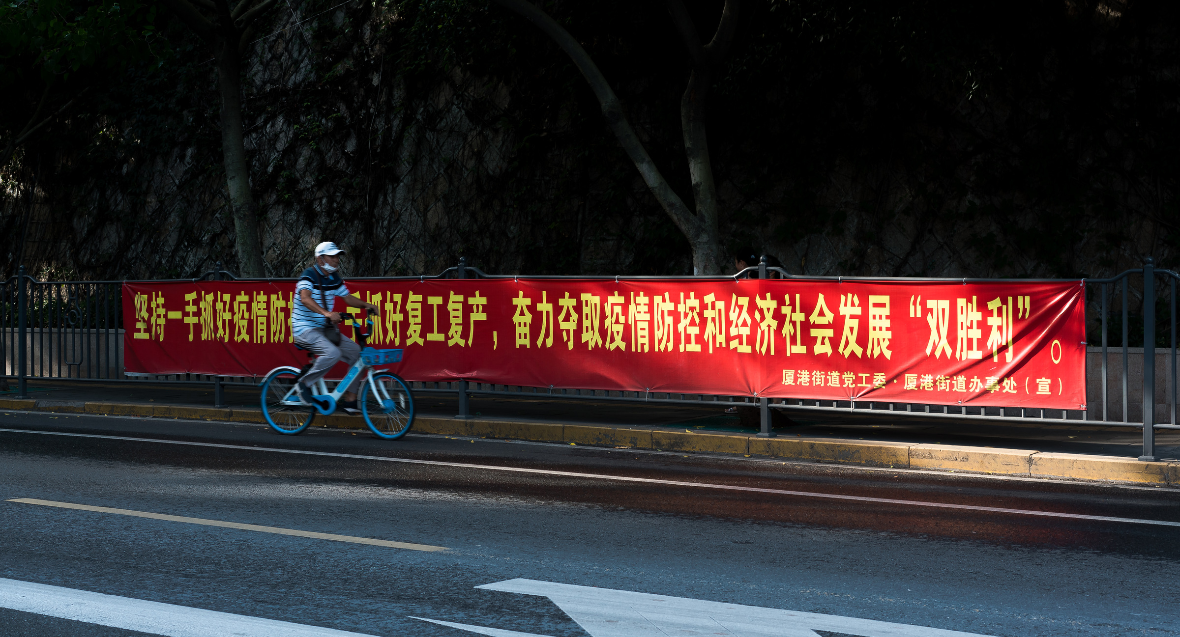 A cyclist passes a red banner about epidemic prevention and the resumption of work.