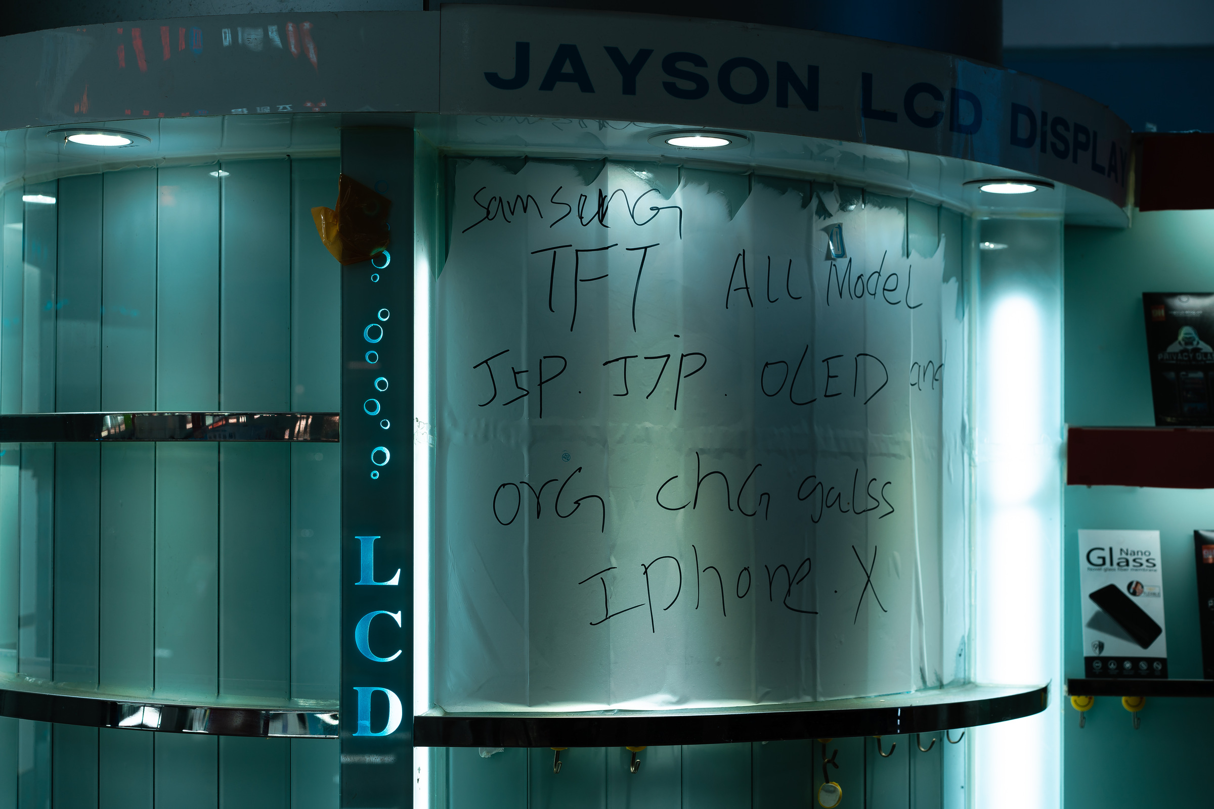 A handwritten display advertises phone screens beneath cool fluorescent light.