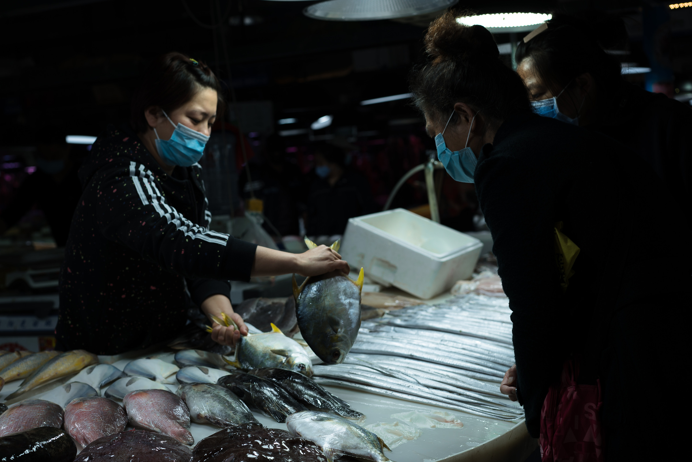 Two masked people lean toward a fish counter during a transaction.