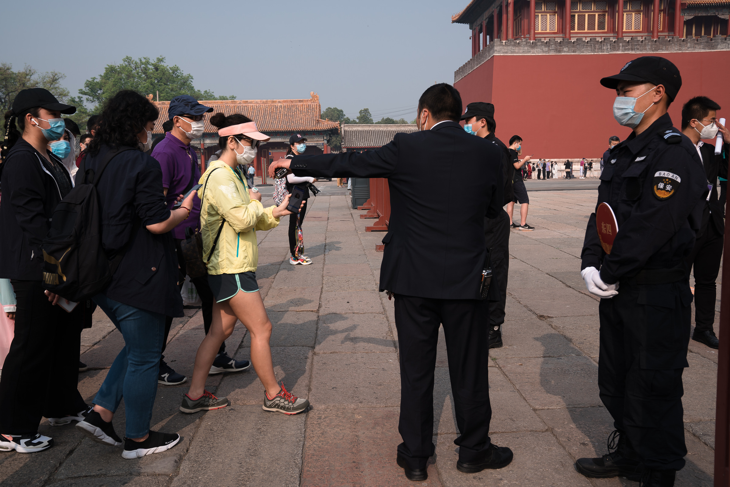 A man extends his arm to direct visitors beside a uniformed guard at the Forbidden City.