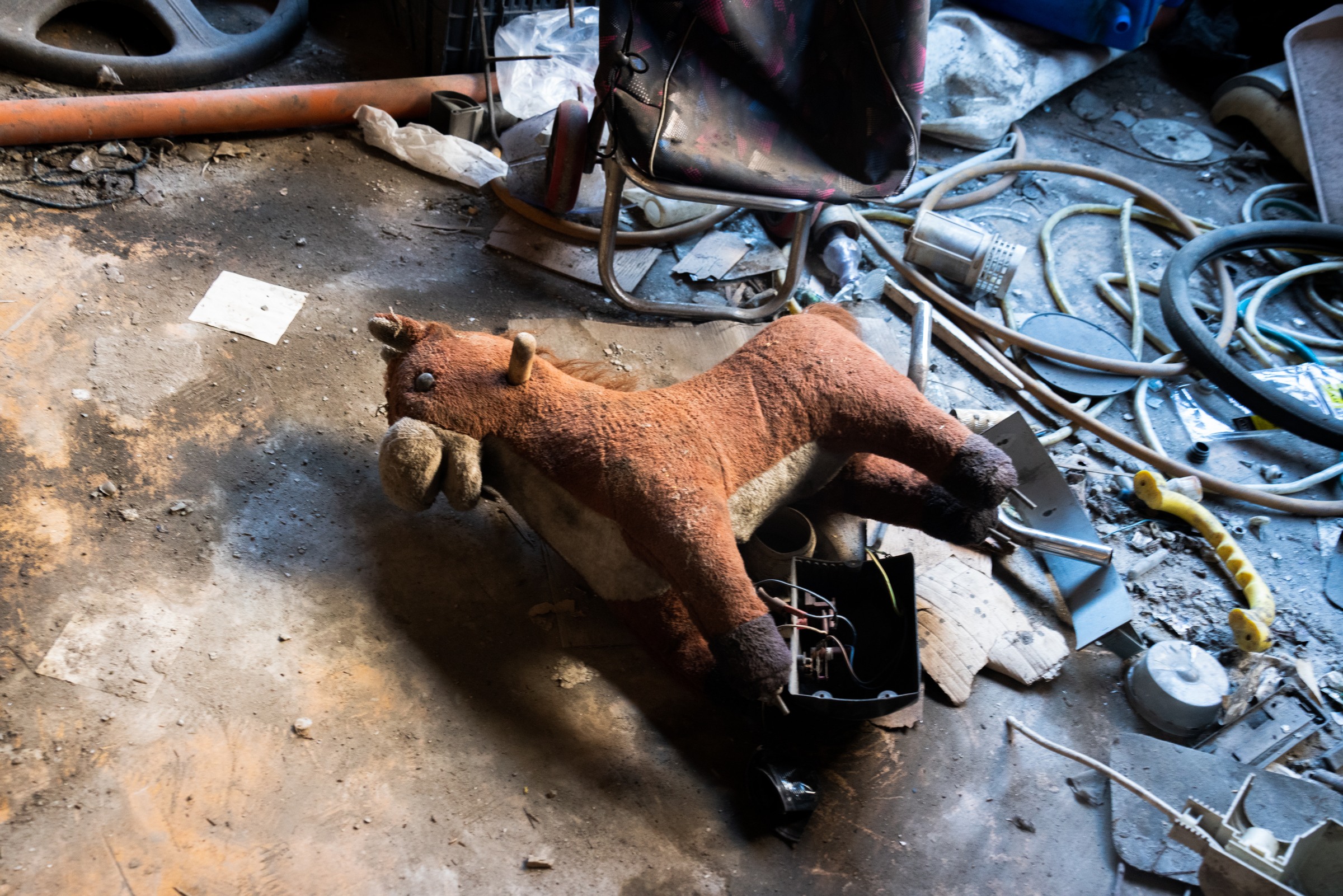 A toy horse lies on a floor among a chair, hoses and scattered objects.
