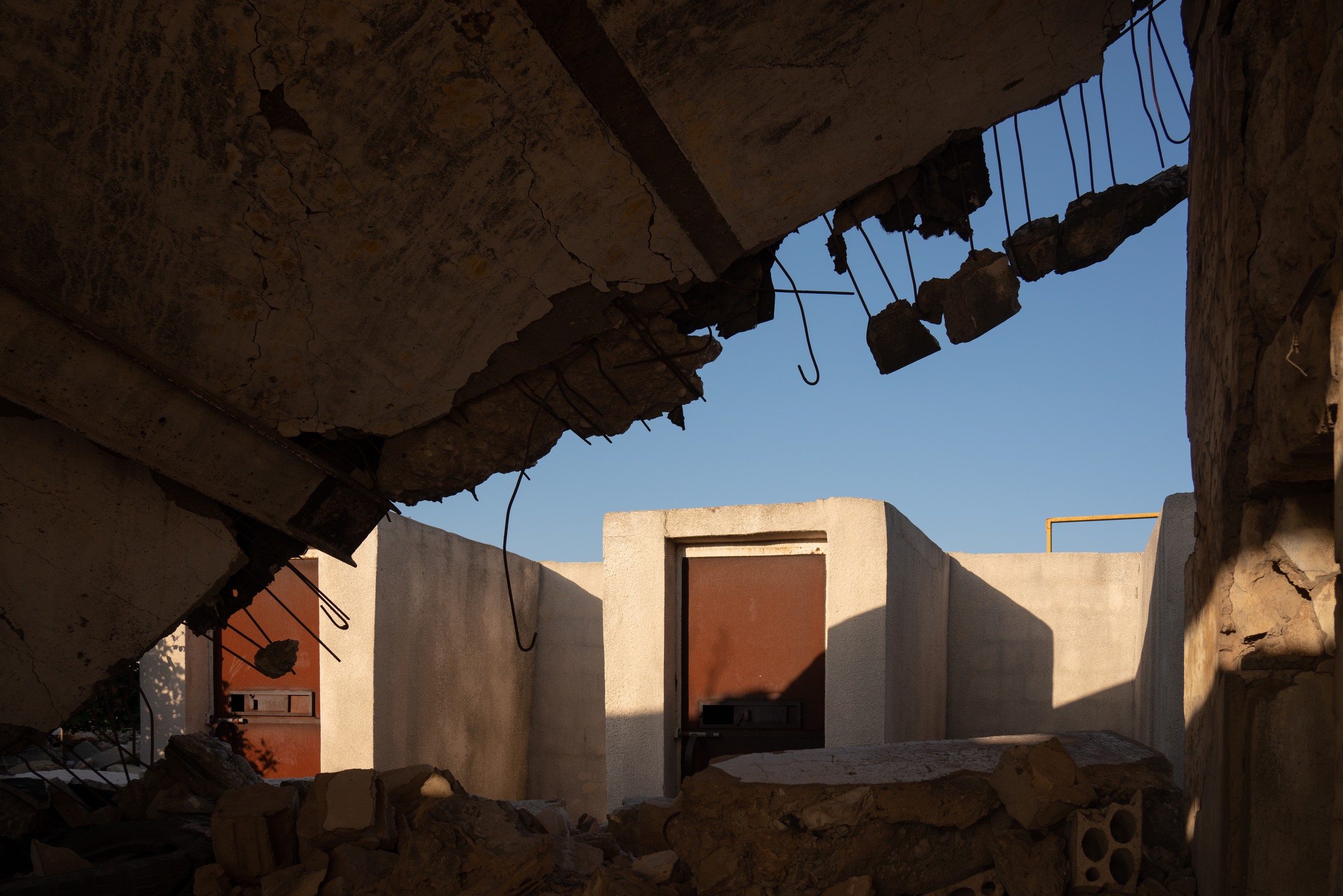 Broken concrete and exposed steel frame blue sky and doorways beyond.