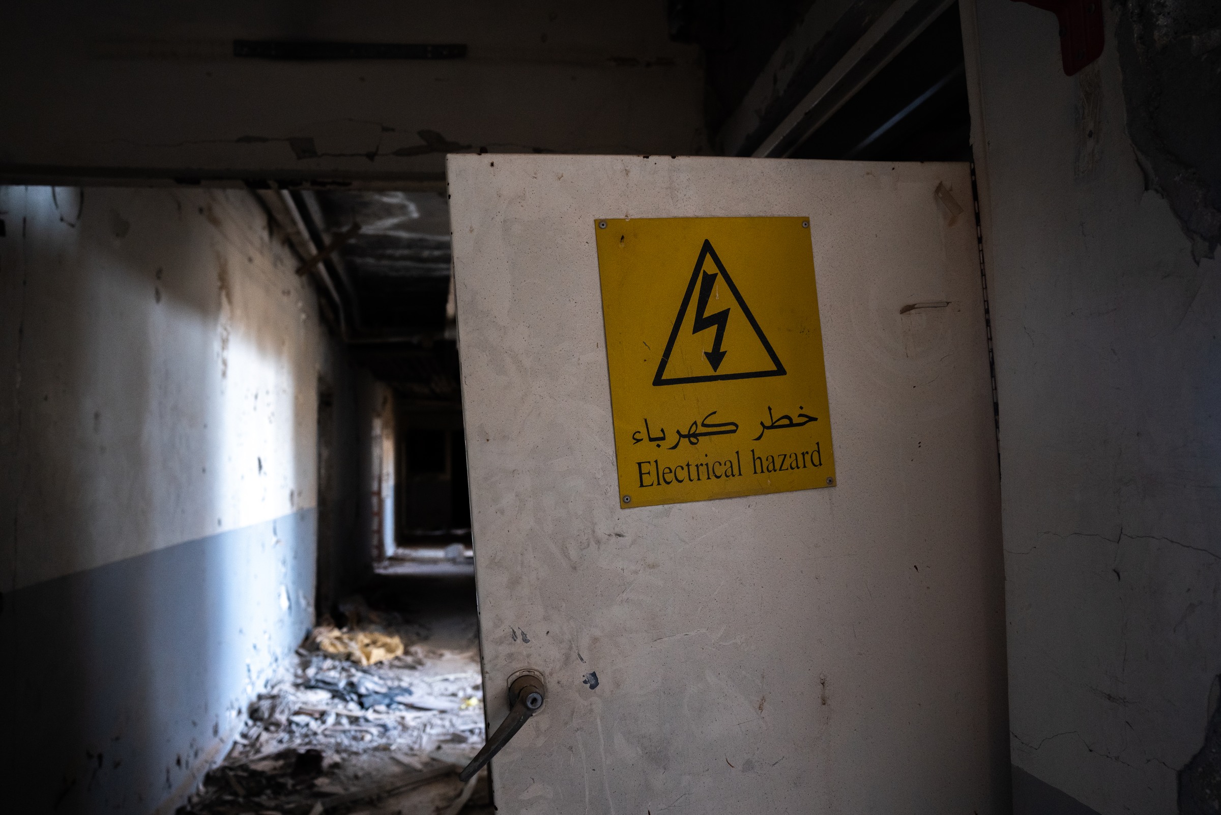 An open door with a yellow electrical warning partly obscures a debris-filled corridor.