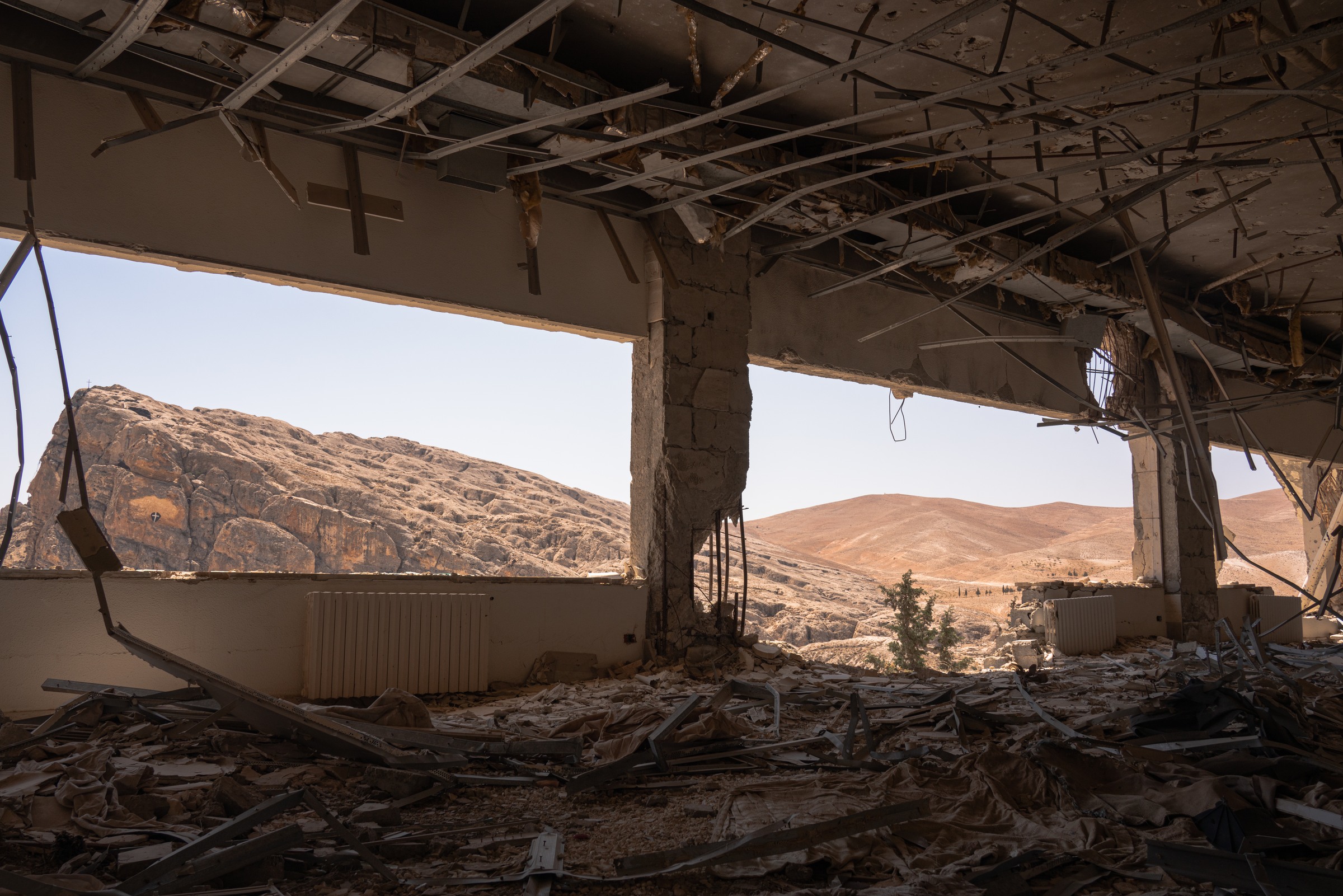 An exposed interior opens onto sunlit mountains beneath a damaged ceiling.
