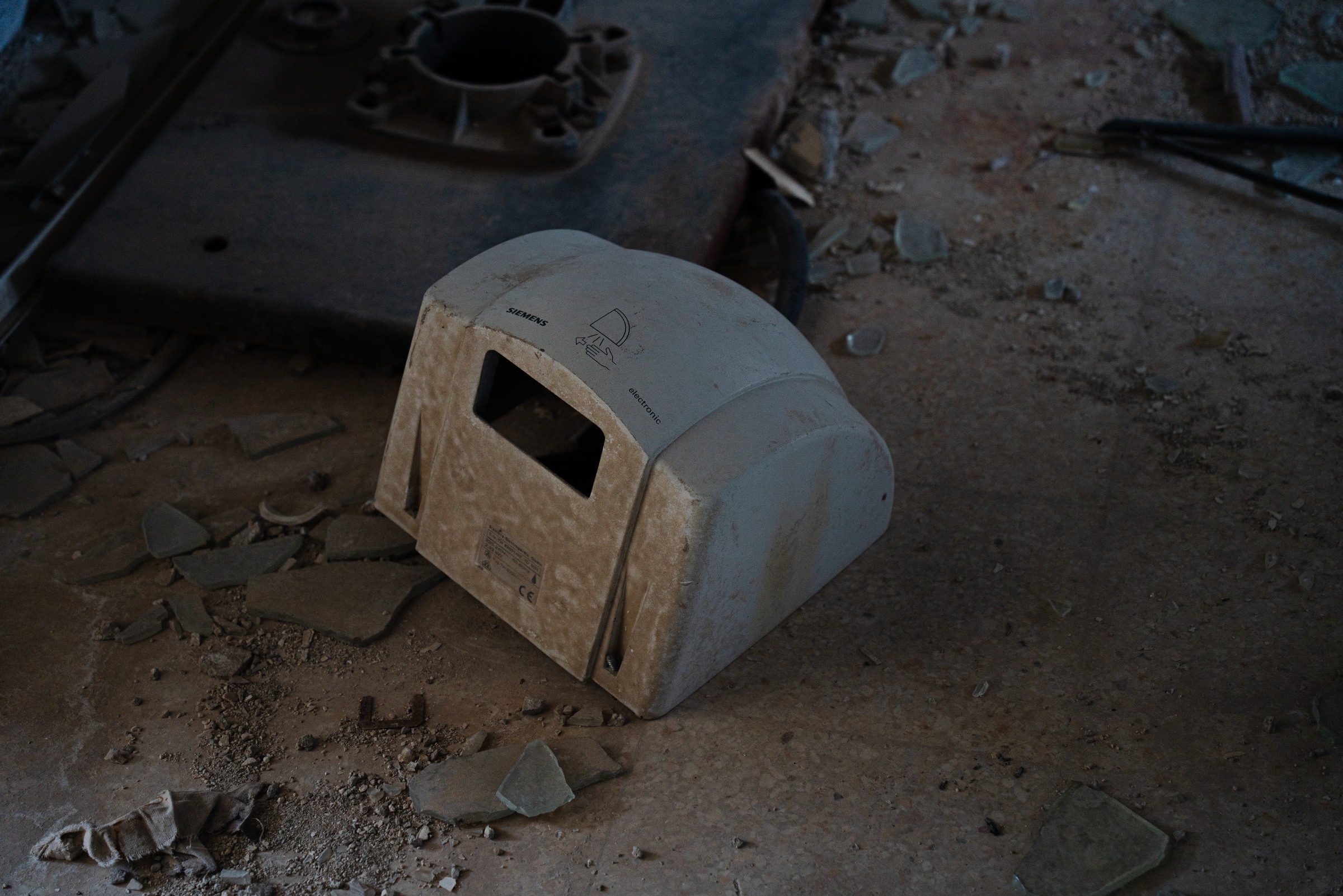A detached hand dryer rests among dust and broken glass.