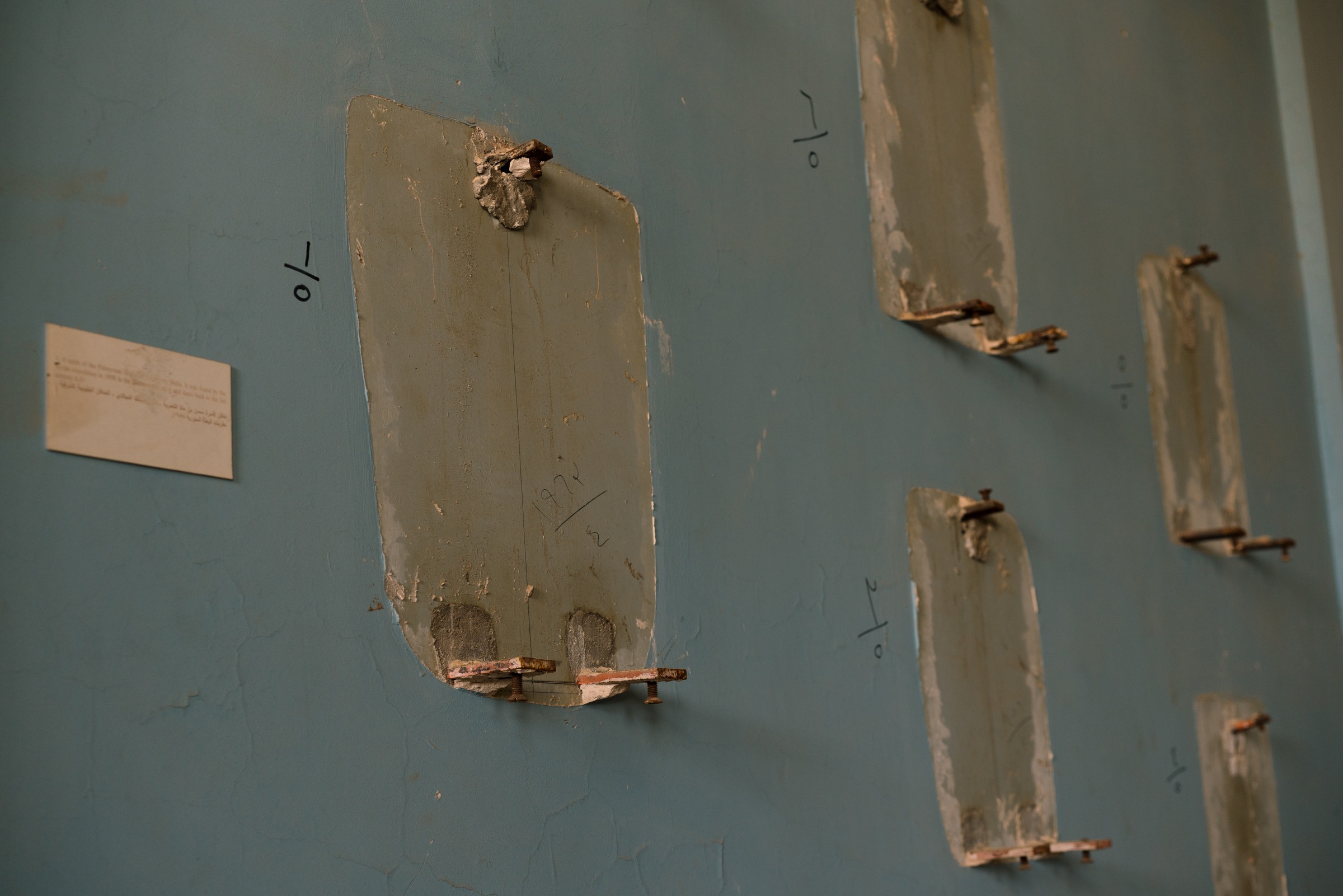 Empty mounts, numbered markings and pale outlines remain on a blue museum wall.