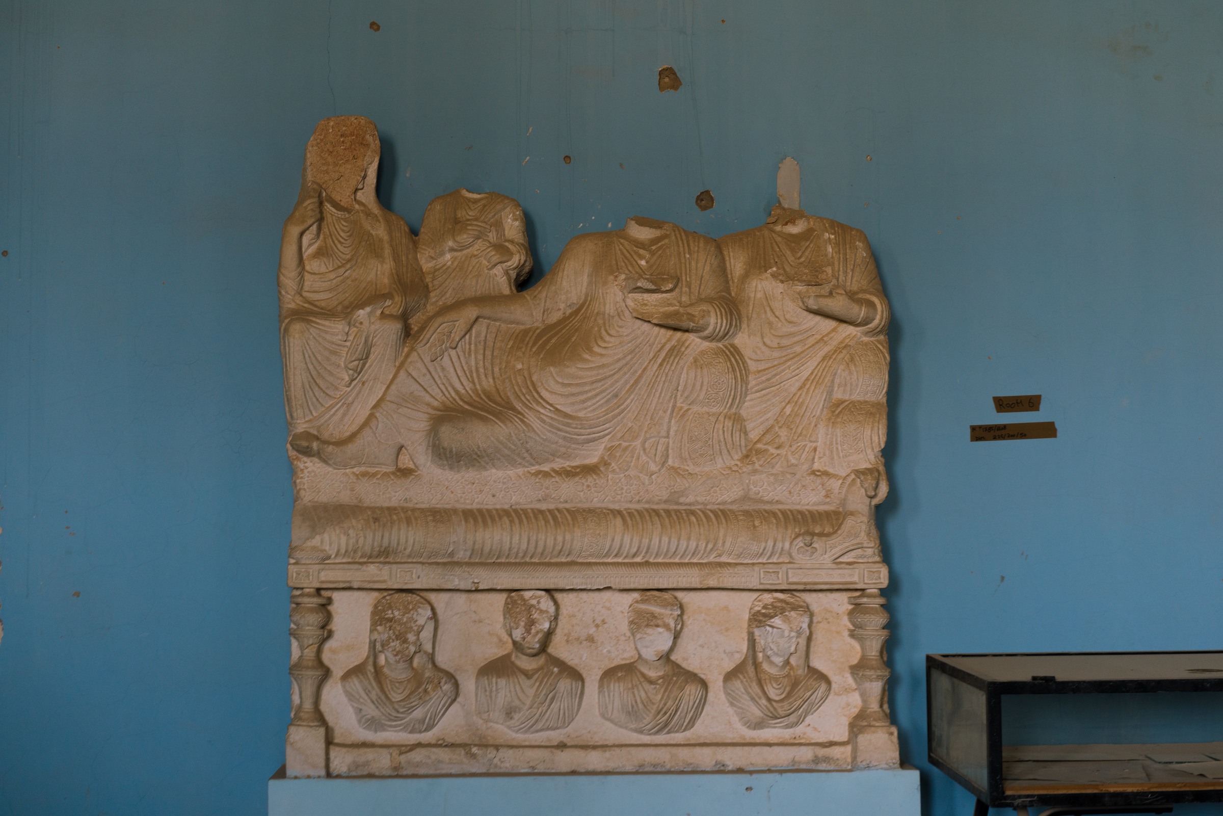 A damaged stone relief stands against a blue wall beside a display case.