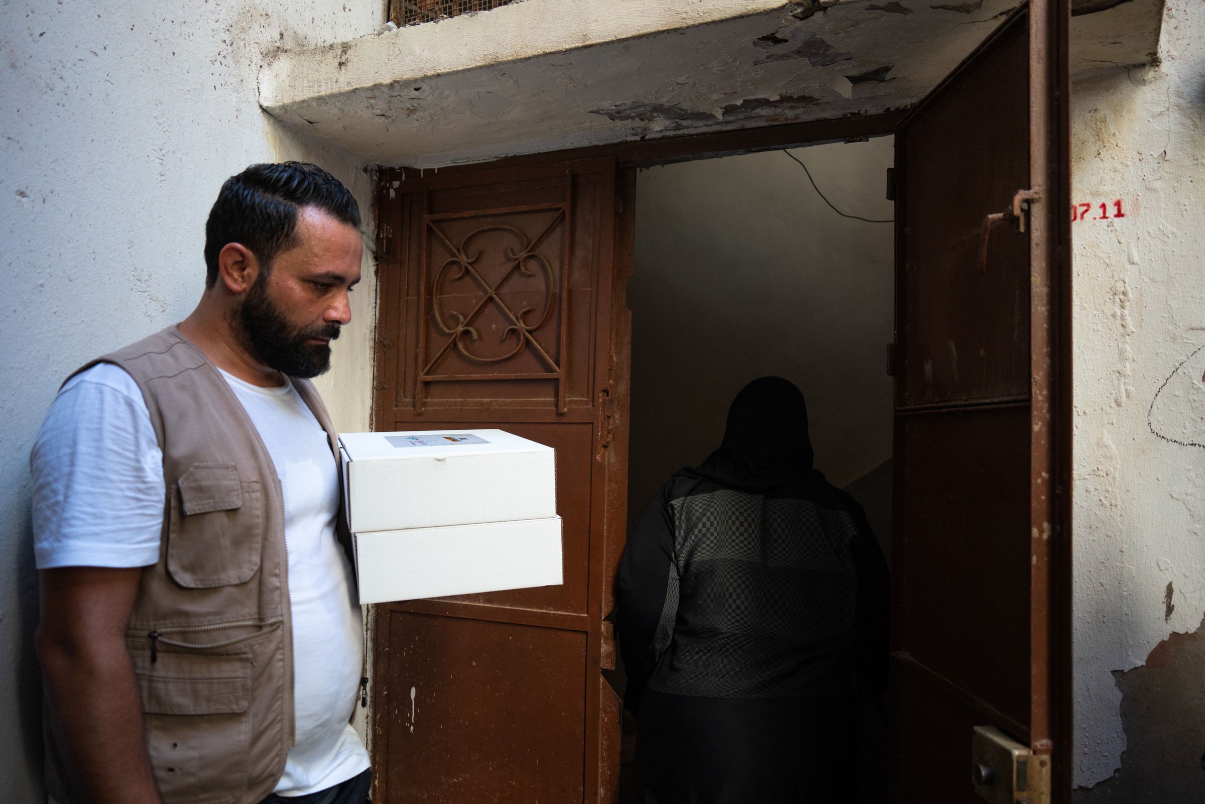 A man holds two white boxes beside a doorway as another person enters.